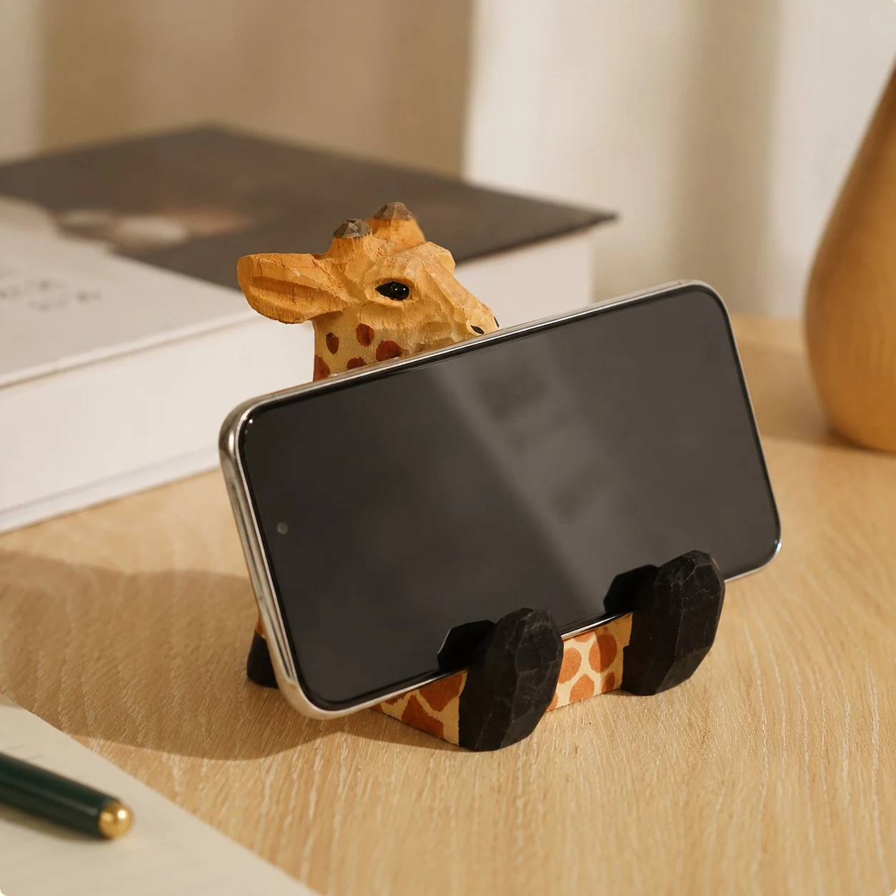 Giraffe wooden phone stand holding a phone on a desk