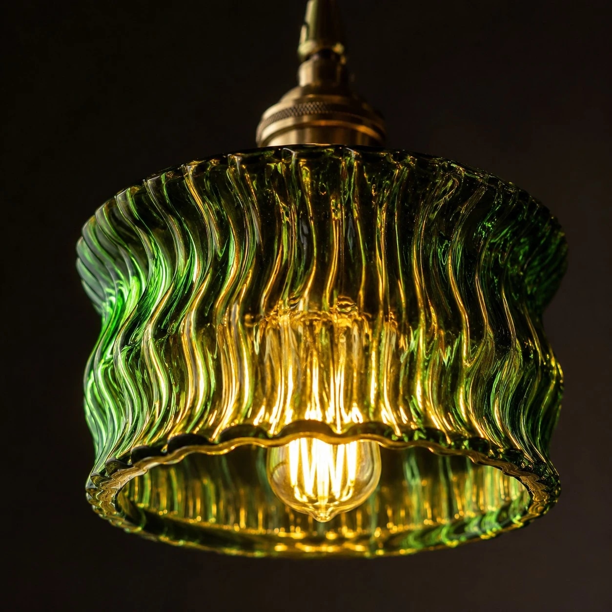 Una luce calda filtra attraverso un paralume a sospensione in vetro verde ondulato.