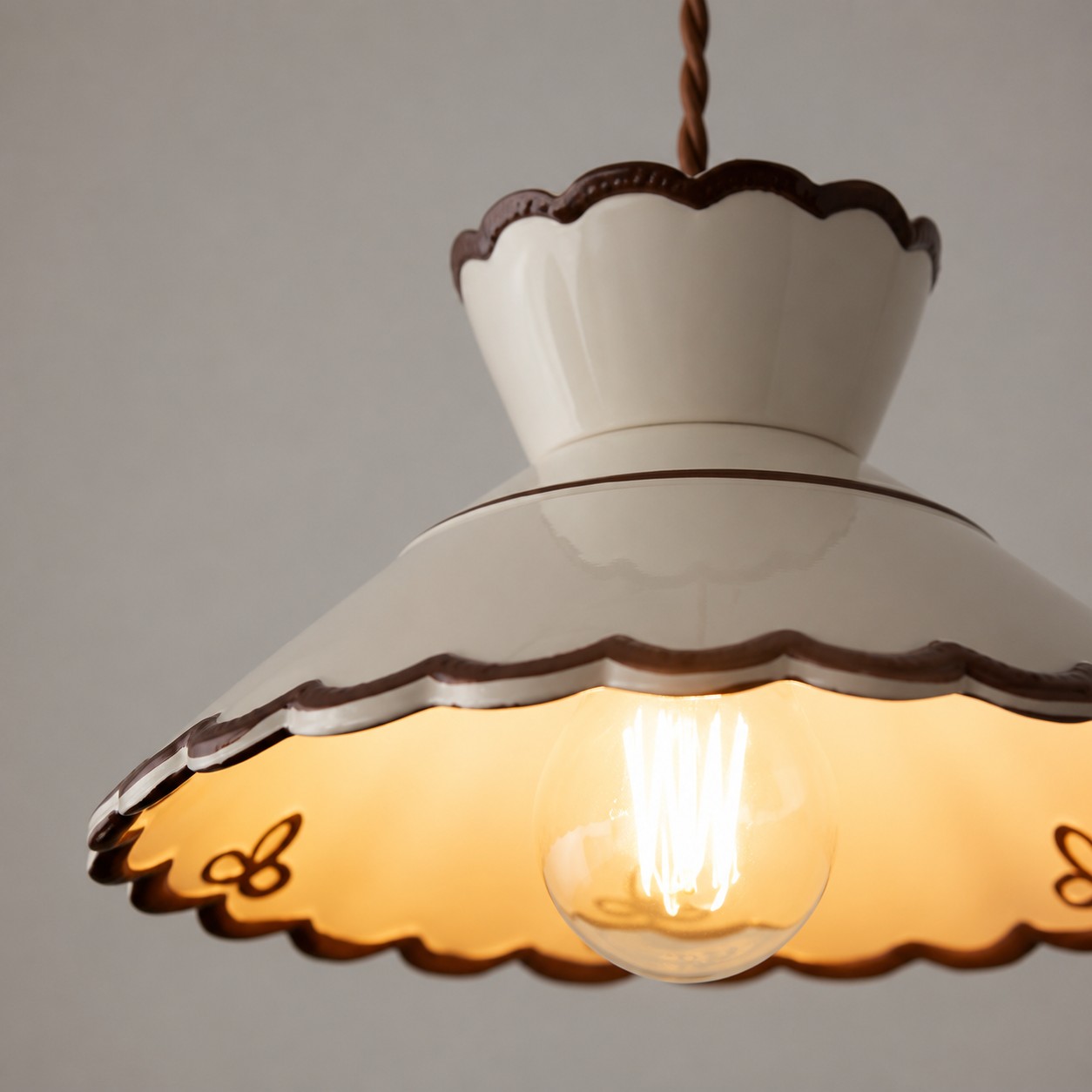 Dettaglio ravvicinato del paralume a sospensione in ceramica color bianco crema con bordo smerlato.