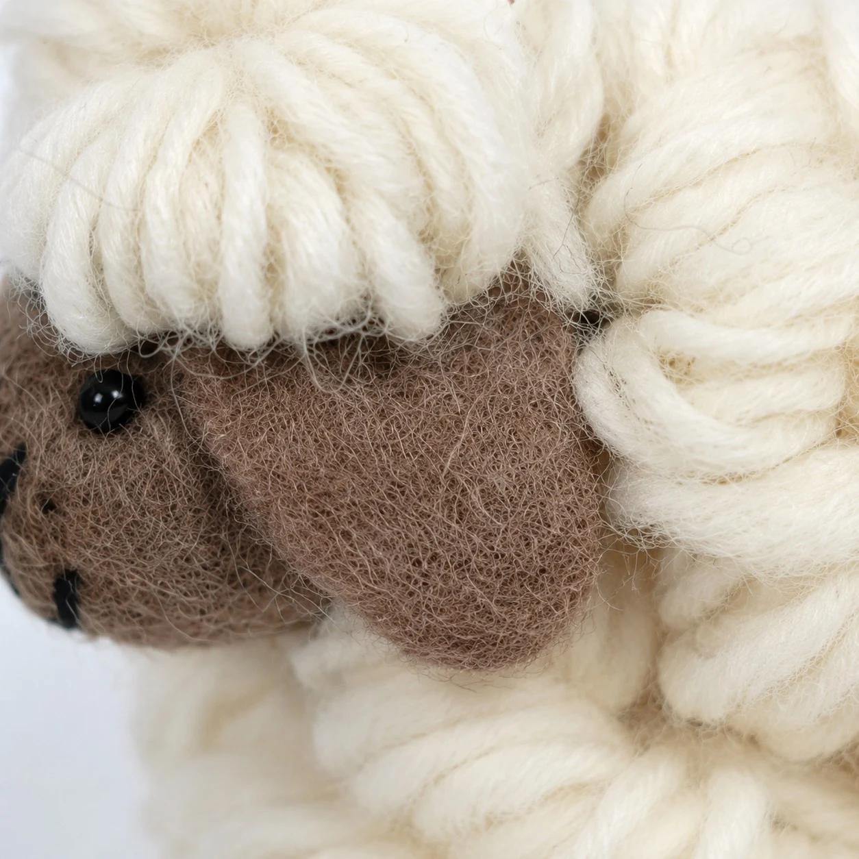 Gros plan sur le visage de mouton en feutre marron et la toison en laine crème