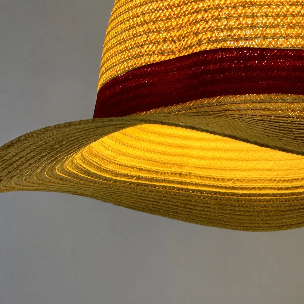 Textura de palha em camadas, aba larga e uma elegante faixa vermelha como destaque.