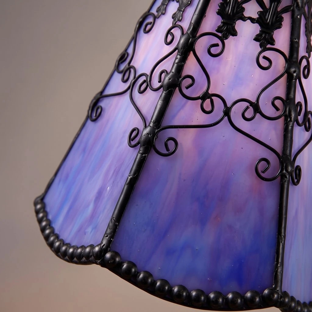 Close-up of purple-blue Tiffany stained glass shade with black scrollwork and beaded edge