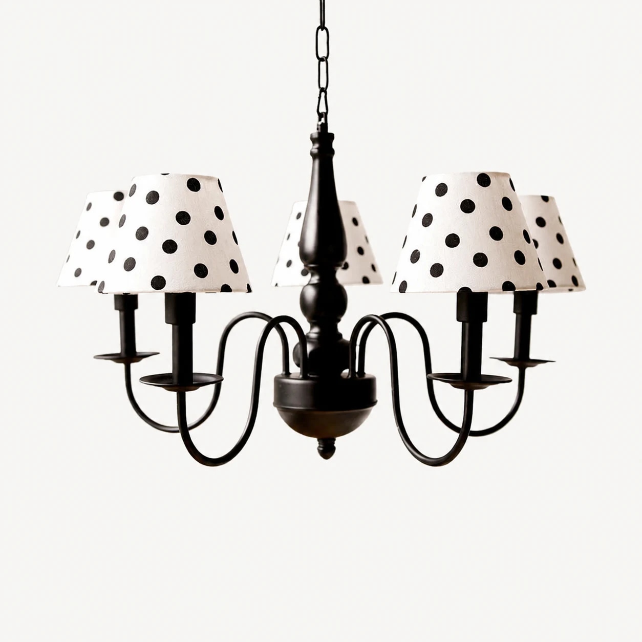 Lustre preto de cinco braços com cúpulas de tecido creme com bolinhas.