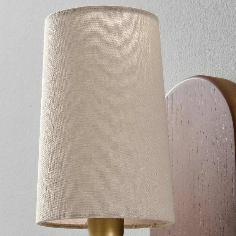 A woven fabric shade diffuses the bulb into a calm ambient glow, making the sconce suitable beside a bed, sofa, console, or narrow hallway wall.
