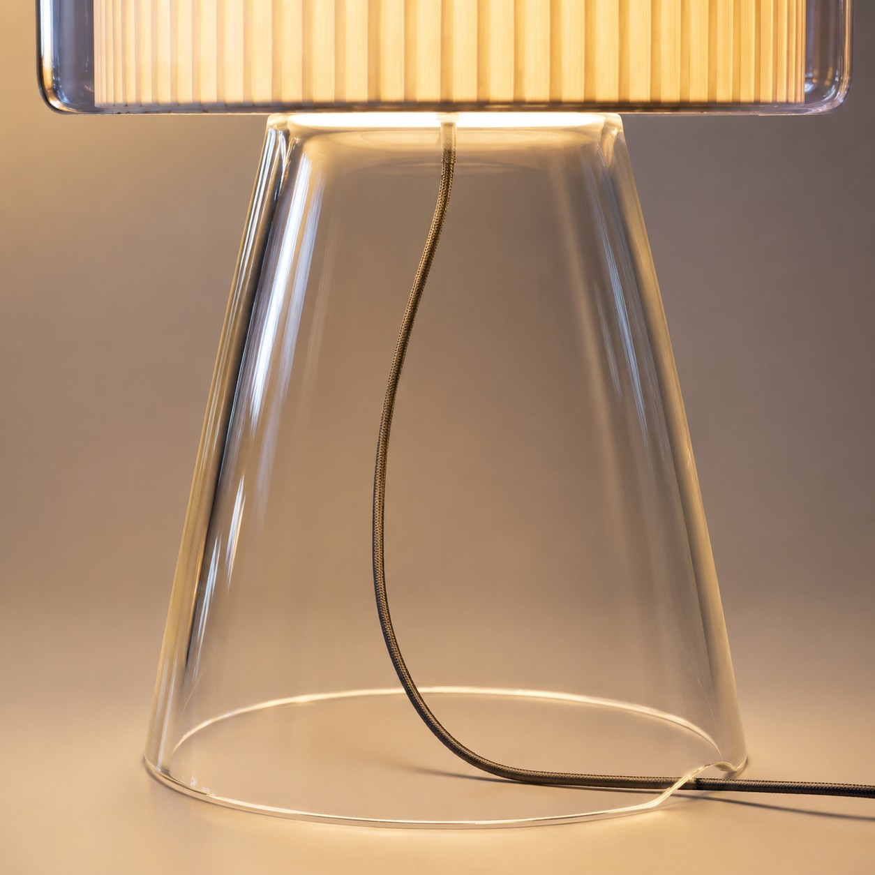 Lampada da tavolo in vetro naturale con paralume in tessuto e dettagli di finitura.